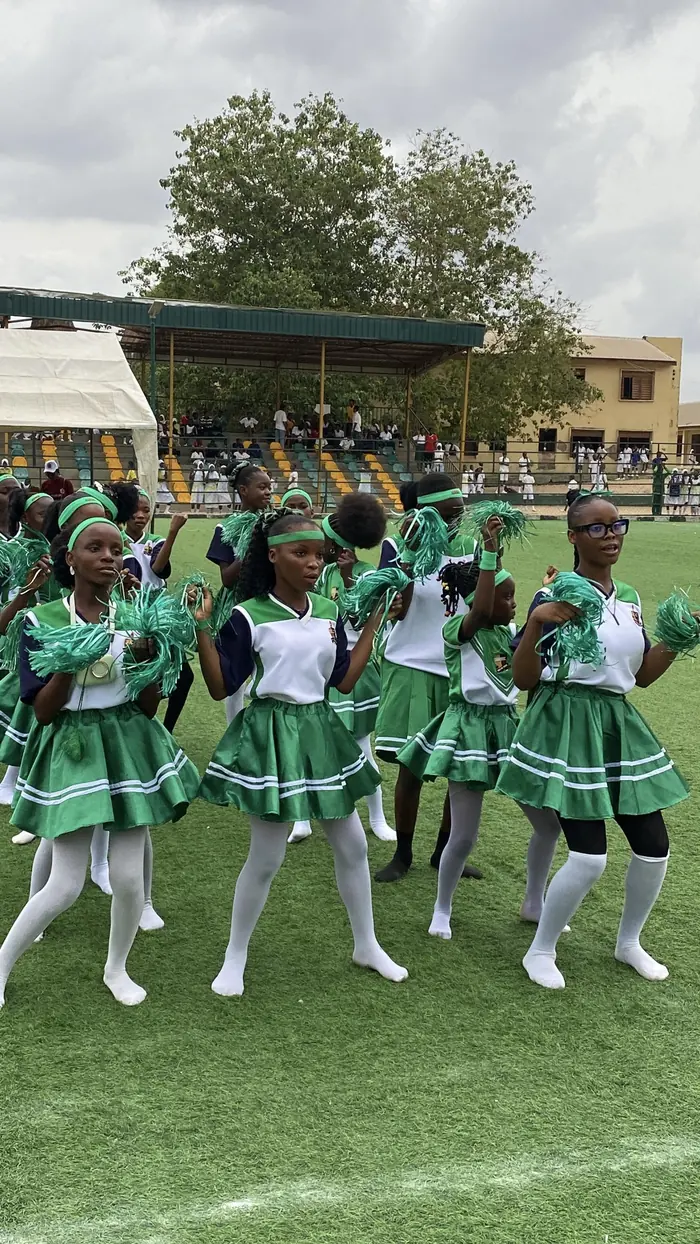 Students in green sports kit performing with pom-poms on a field